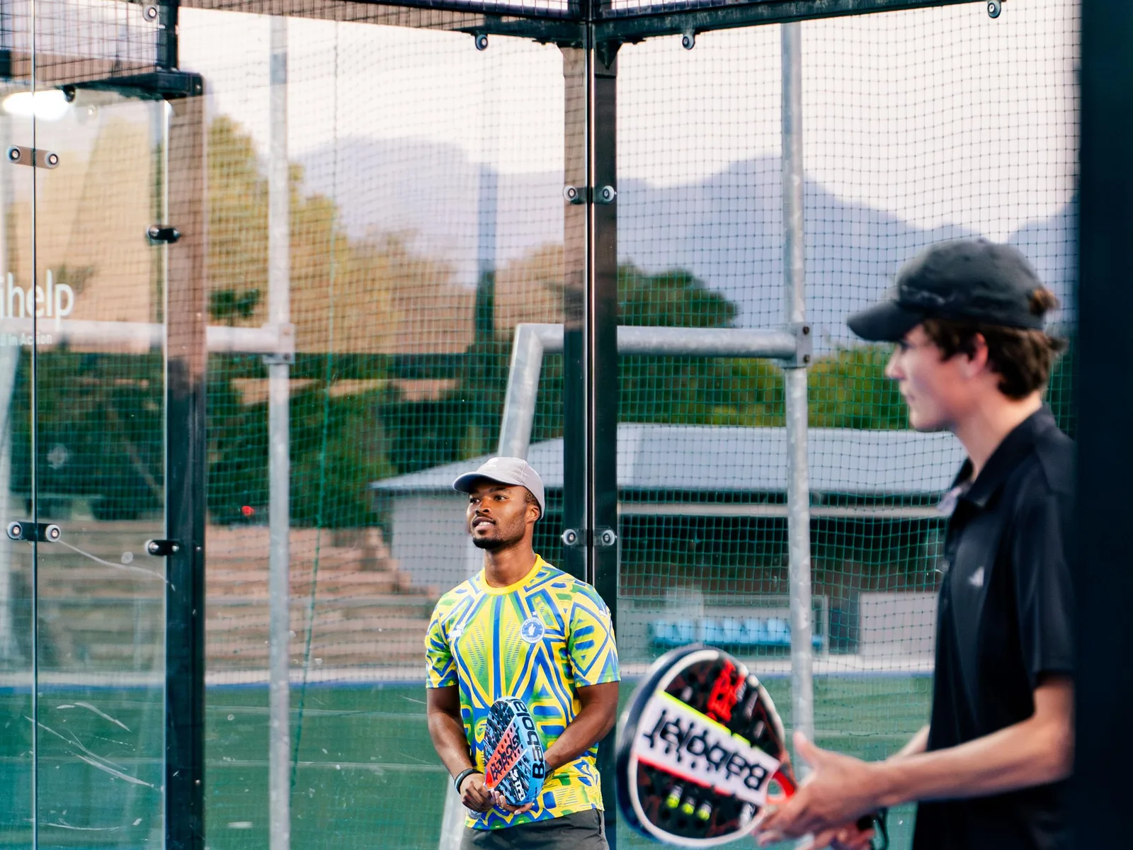 Two players at the net between points, rackets down, the mountains behind the court