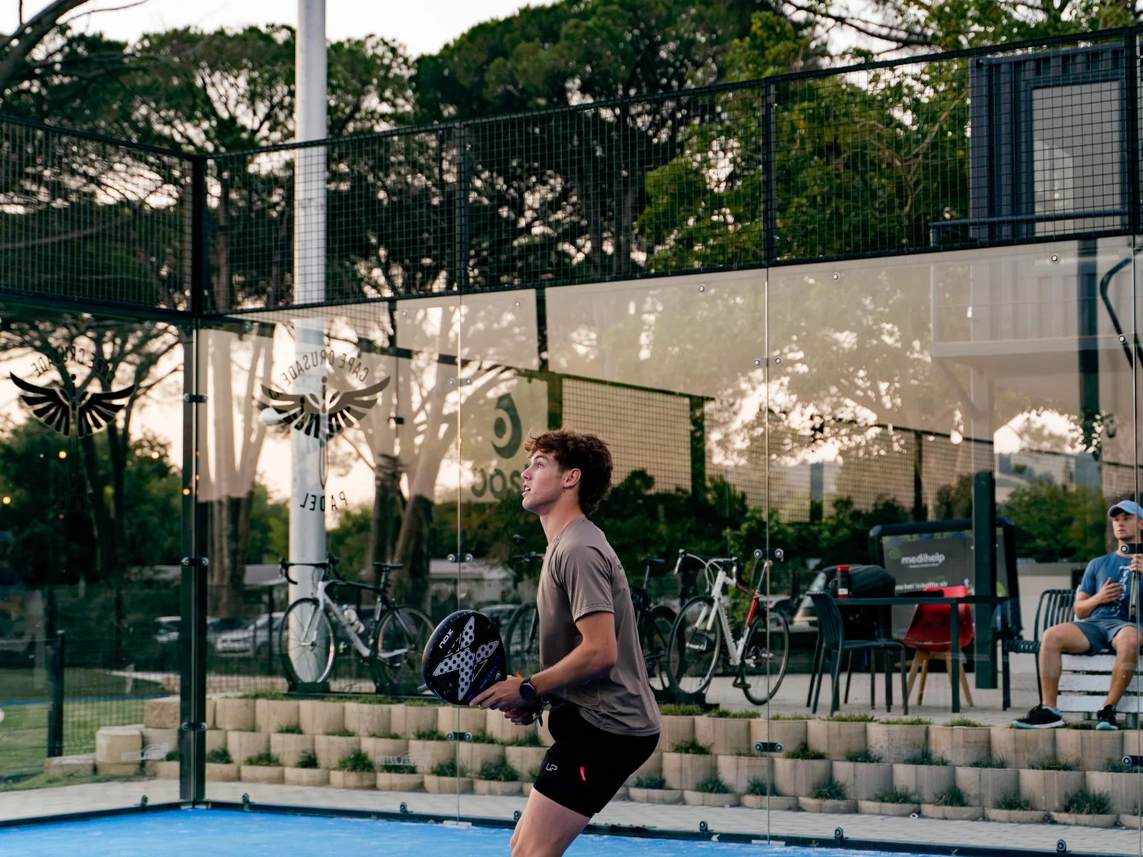 A wide view of the court from behind the glass, a point in play under the trees