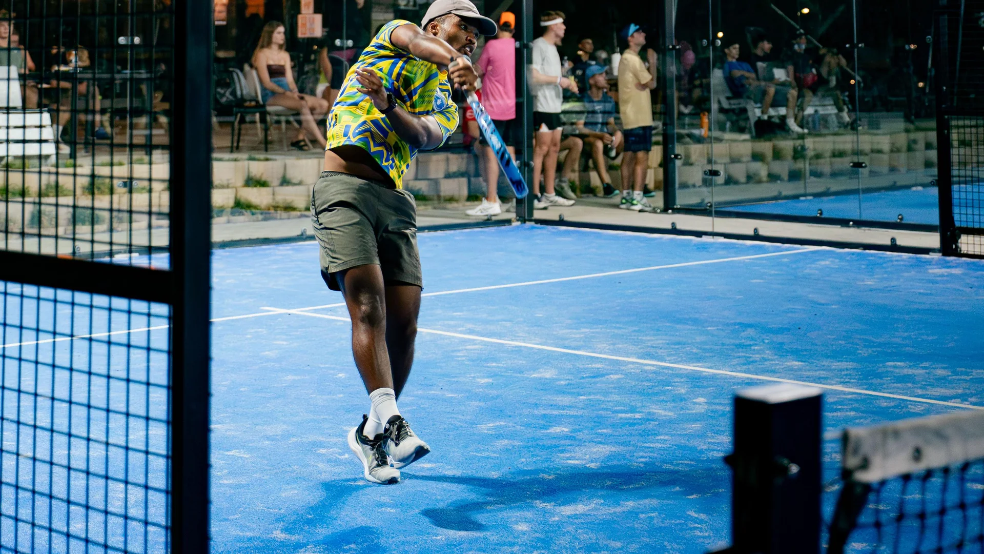 A player mid-shot on the blue court, spectators watching from the steps