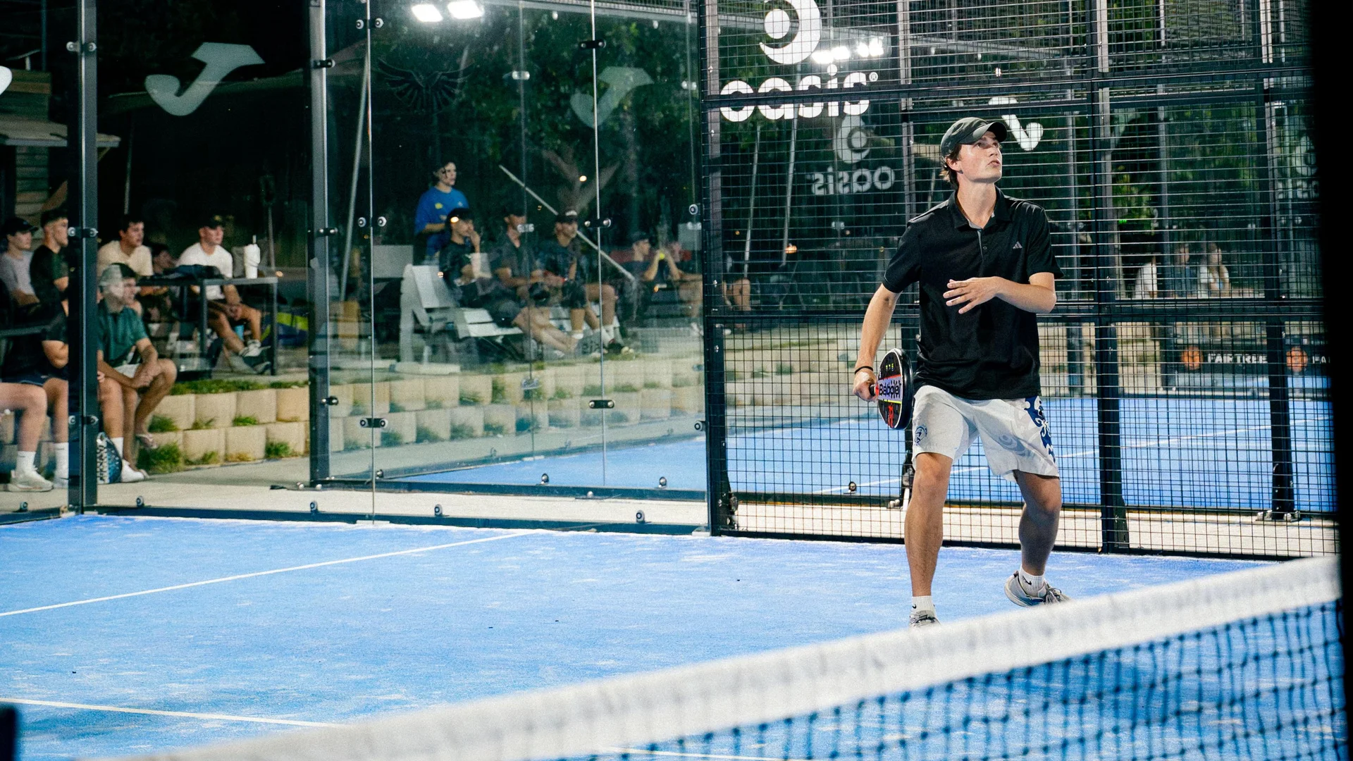 A player on court under the floodlights, people watching courtside