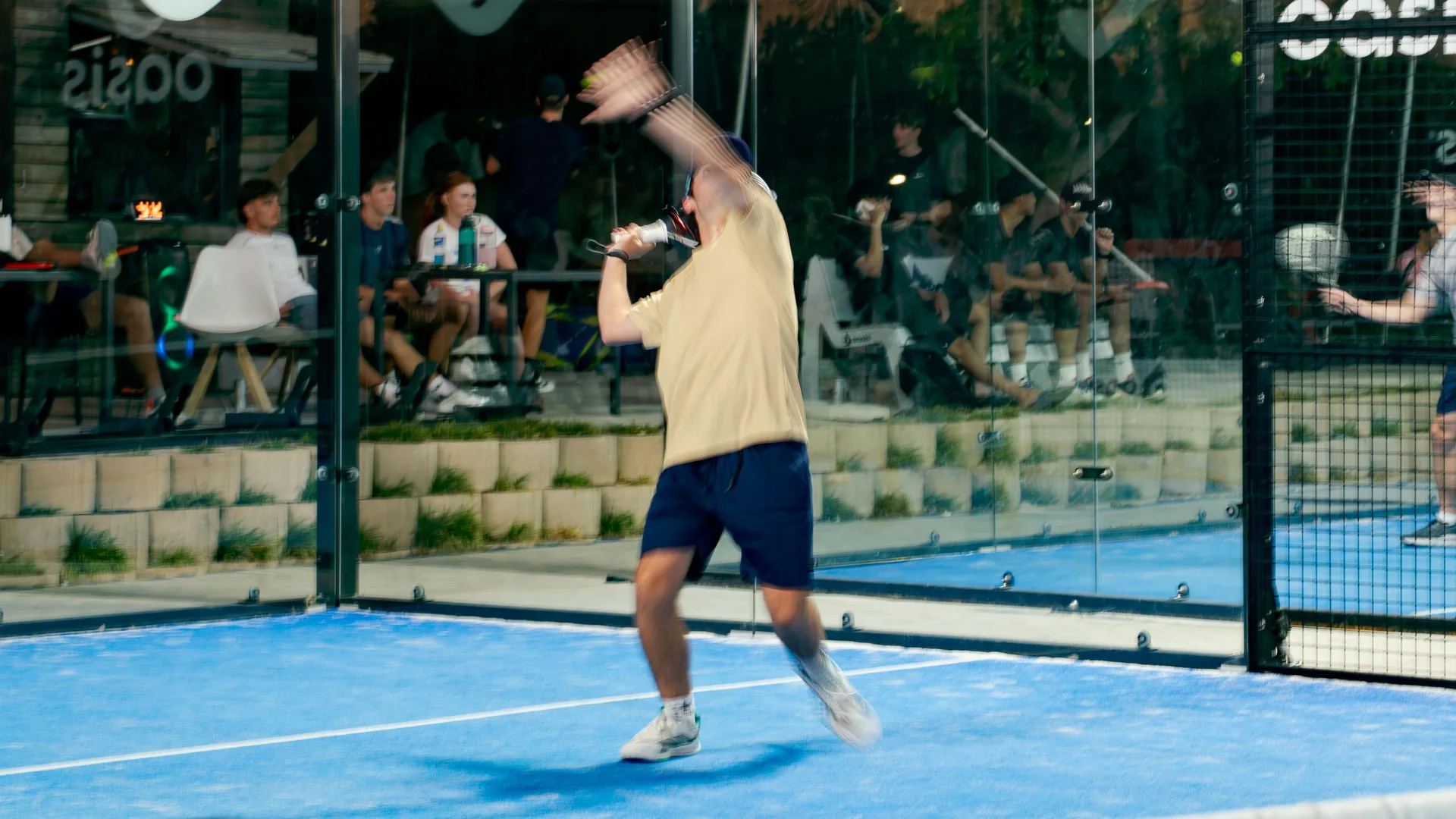A player serving while spectators watch from the courtside seats